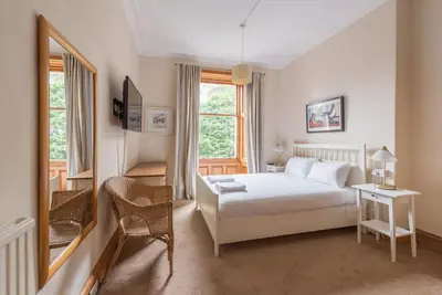 a bedroom with a bed and a chair and a window at Beautiful 2 Bed 2 Bath Flat overlooking Meadows Park in Edinburgh