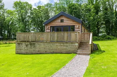a small cabin with a deck on the grass at Squirrel Lodge 42 with Hot Tub in Newton Stewart
