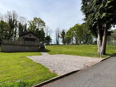 a building on the side of a field with a tree at Squirrel Lodge 43 with Hot Tub in Newton Stewart