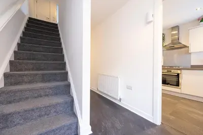 a staircase in a home with white walls and a kitchen at Stylish 3BR Home with Garden & Free Parking - Near O2 Academy & City Centre in Glasgow
