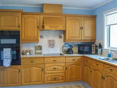 a kitchen with wooden cabinets and a stove top oven at Lowesmuir Cottage in Cumnock