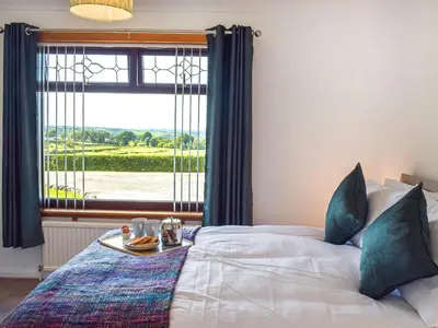 a bed with a tray of food on it in front of a window at Lowesmuir Cottage in Cumnock
