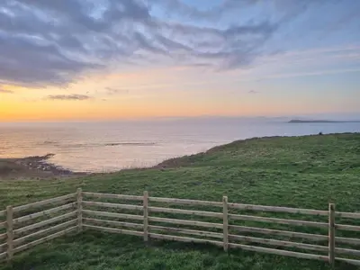 a fence on a hill next to the ocean at North Muasdale Farm - Byre View in Muasdale