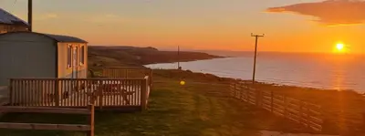 a sunset over the ocean next to a building at North Muasdale Farm - Byre View in Muasdale
