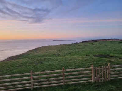 a fence on a hill next to the ocean at North Muasdale Farm - Byre View in Muasdale