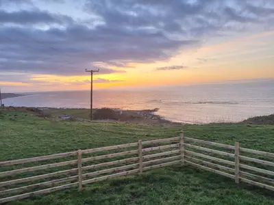 a sunset over the ocean with a fence at North Muasdale Farm - Byre View in Muasdale