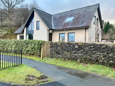 a house with a stone wall and a fence at The Beach House Loch Lomond in Luss