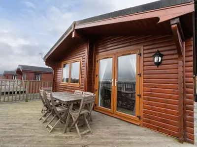 a wooden cabin with a table and chairs on a deck at Chalet Loch Leven Lodge 10 by Interhome in Kinross