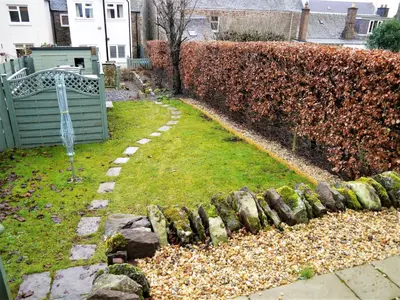a garden with a fence and a lawn with rocks at Greenbrae East in Crieff
