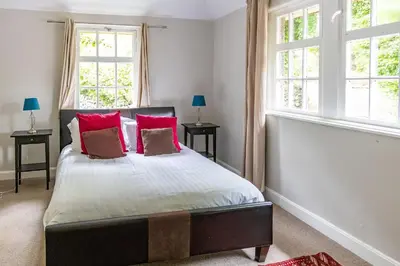 a bedroom with a bed with red pillows and two windows at Newholme House in Stirling