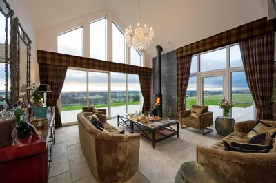 a living room with couches and a table and windows at Kipney Farmhouse with hot tub in Perth