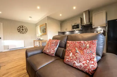 a living room with a brown couch and a kitchen at Bluebell Lodge 11 with Hot Tub in Newton Stewart