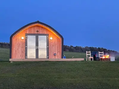 a wooden barn in a field with a grill at Hedgehog's Nest in Bathgate