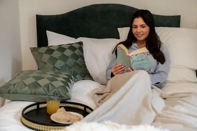 a woman sitting on a bed reading a book at Finnieston 1-Bed - Walk to Hydro & Bars - Sleeps 2 in Glasgow
