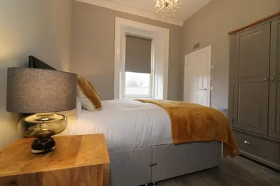 a bedroom with a bed and a table with a lamp at Signature - Linden House Flat 3 in Airdrie