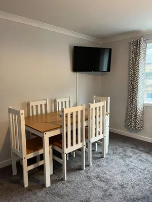a dining room table with chairs and a television on the wall at Breadalbane Apartment in Oban