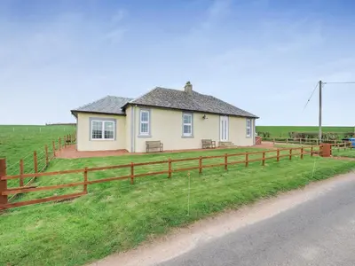 a house on the side of a field with a fence at Kerrytonlia Cottage in Mountstuart