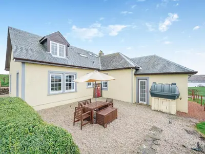 a house with a patio with a table and an umbrella at Kerrytonlia Cottage in Mountstuart