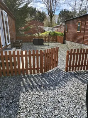 a yard with two wooden fences and a house at Red Squirrel Lodge in Auchterarder