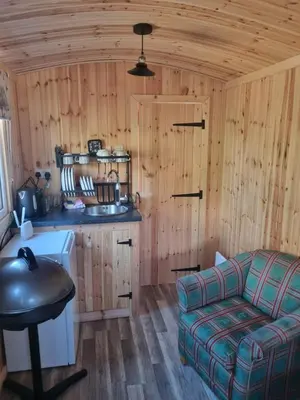 a room with a couch and a kitchen in a cabin at Blair snug hut in Kelty