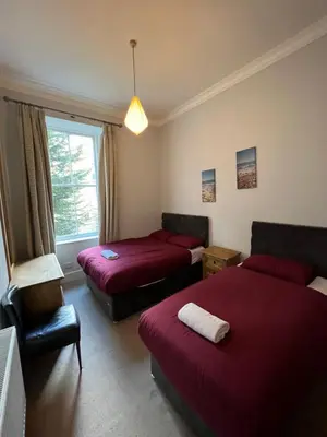 a bedroom with two beds and a chair and a window at Sauchiehall Street West End Apartment in Glasgow