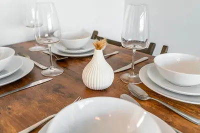 a wooden table with a white vase and plates and wine glasses at Quirky, Family Home in Glasgow in Cardonald