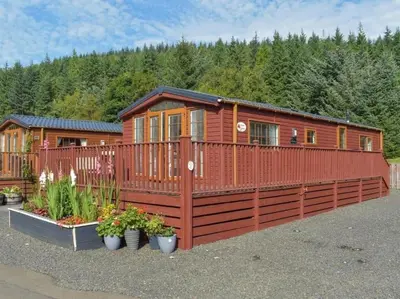a large wooden cabin with a fence and flowers at Poppy Lodge Glendevon Scotland in Glendevon