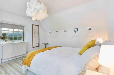 a white bedroom with a bed and a chandelier at Sleeps 10. The Old pink library by loch and river in Lochearnhead