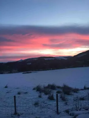 a sunset over a snowy field with a fence at Sleeps 10. The Old pink library by loch and river in Lochearnhead