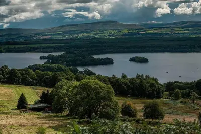 a view of a lake with trees and a house at The Mews - a cottage with a spectacular lake view in Port of Menteith