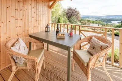 a table and two chairs on a deck with a view at The Stable - cottage with a spectacular lake view in Port of Menteith
