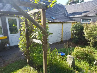 a garden with a wooden sign in front of a house at BARHOLM CROFT Holiday Cottage in Creetown