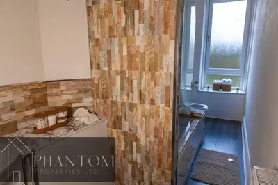 a bathroom with a tiled wall with a sink at Complex Suite in Glasgow