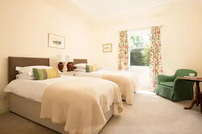 a white bedroom with two beds and a window at Mossfennan House in Drummelzier