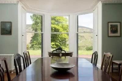 a dining room with a table and a large window at Mossfennan House in Drummelzier