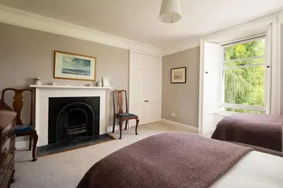 a bedroom with a fireplace and two beds and a window at Mossfennan House & Annexe in Drummelzier