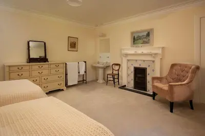 a bedroom with a bed and a chair and a fireplace at Mossfennan House & Annexe in Drummelzier