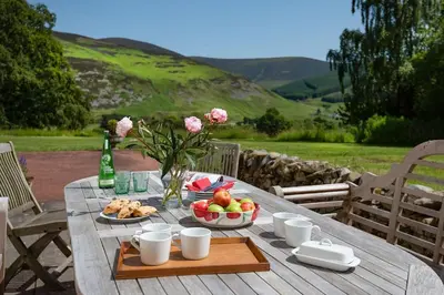a picnic table with a bowl of fruit and a bottle of wine at Mossfennan House & Annexe in Drummelzier
