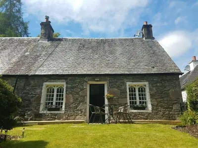 an old stone cottage with a black door and windows at Historic cottage next to loch lomond Luss in Alexandria