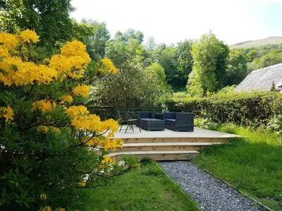 a garden with two benches on a wooden deck at Historic cottage next to loch lomond Luss in Alexandria